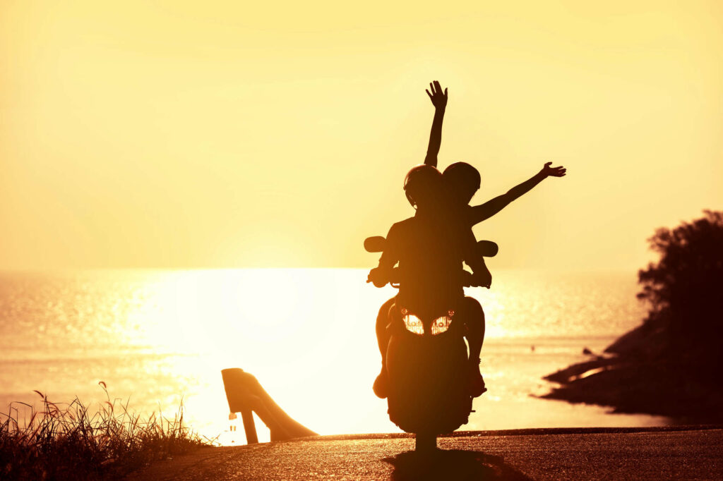 unrecognizable couple on scooter against sunset sea